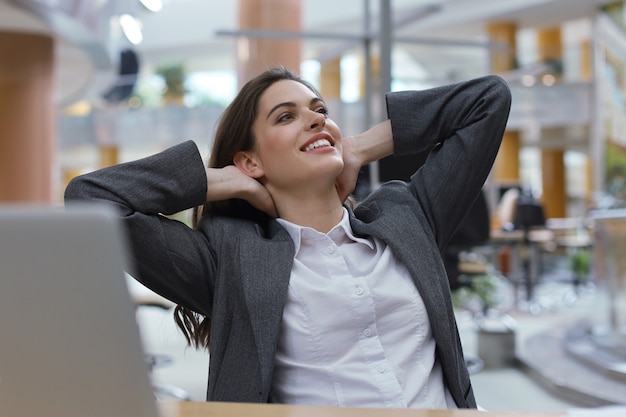 Young businesswoman sitting at office desk hold hands behind head relaxing feels good.