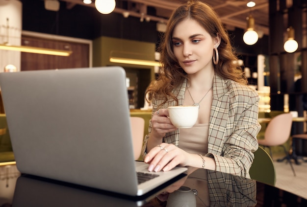 Young businesswoman in smart casual wear drinks coffee and working on laptop