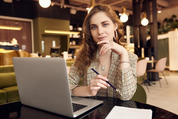 Young businesswoman in smart casual wear makes notes in a notebook in a coffee shop interior