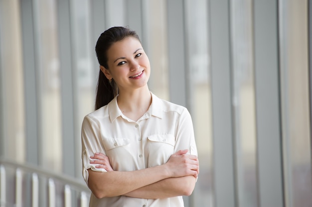 Young businesswoman standing by window with crossed arms.