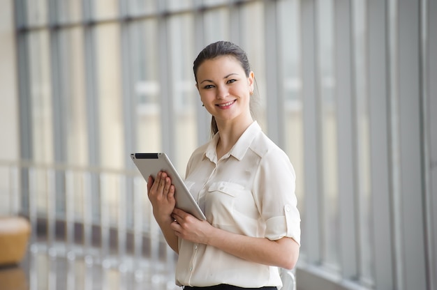 Photo young businesswoman standing by the window with tablet computer.