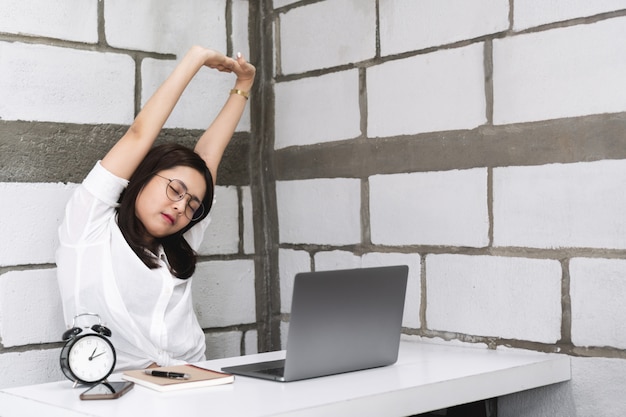 Young businesswoman stretching her arms and body for relaxing while working in office with laptop.