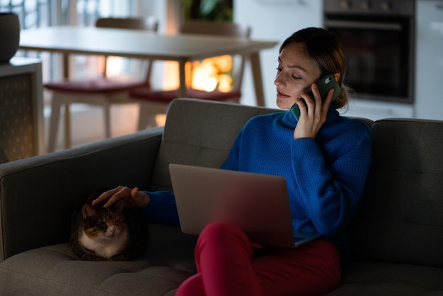 Young businesswoman stroking cat head on sofa talks with colleague discussing business project