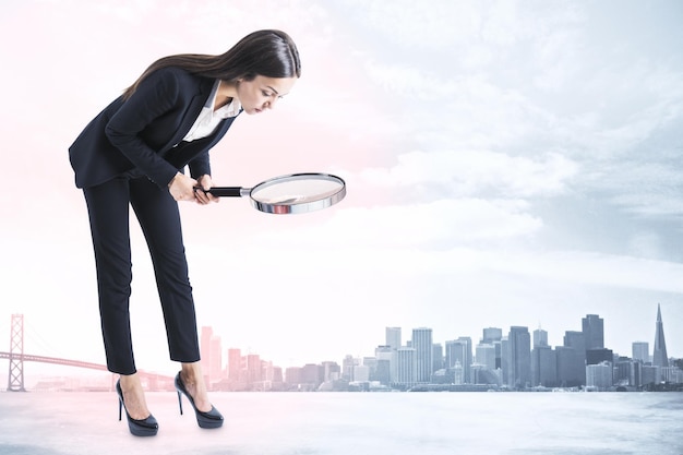 Young businesswoman in suit using magnifier