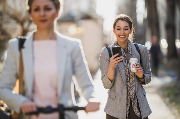 A young businesswoman using a smartphone while having a coffee break and walking through the city.