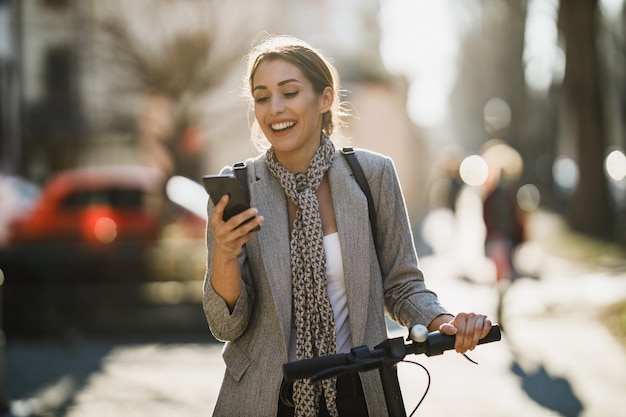 A young businesswoman with an electric push scooter going to work and using smartphone.