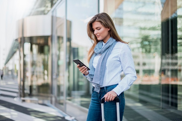 Young businesswoman with suitcase looking at smartphone