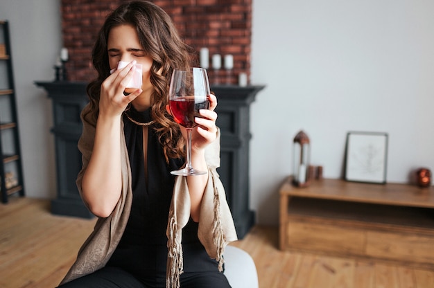 Young businesswoman work at home. Sick model hold glass of red wine in hand. Tissue cover nose. Sick ill woman caught cold and virus. Sickness.