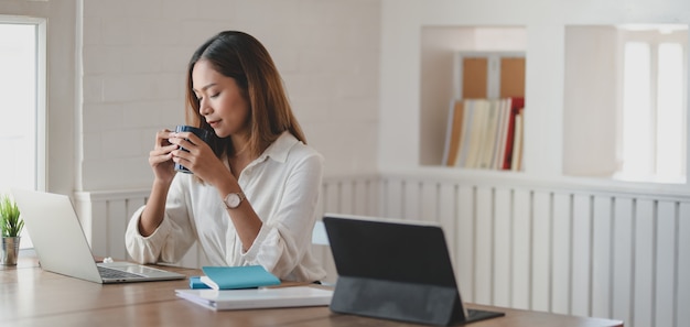 young businesswoman working on her project and drinking a cup of coffee in modern office