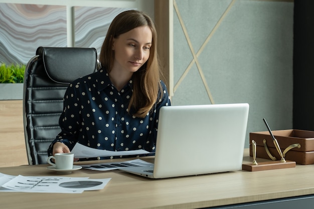 Young businesswoman working online checking mail on laptop organizing working process in office