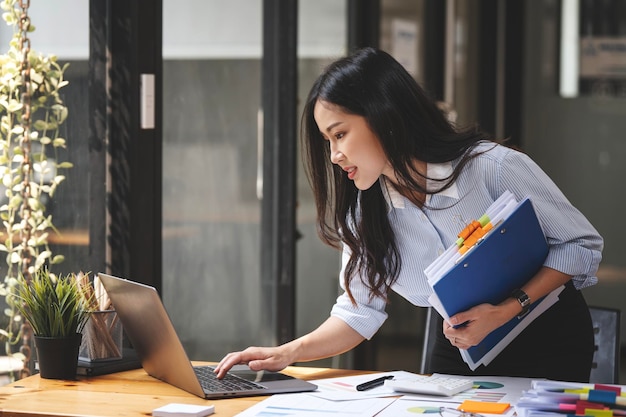 Young businesswoman working with documents in office standing at work table with laptop serious employee checking financial report project statistics reading correspondence