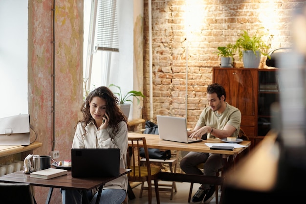 Young busy female freelancer in casualwear talking on mobile phone