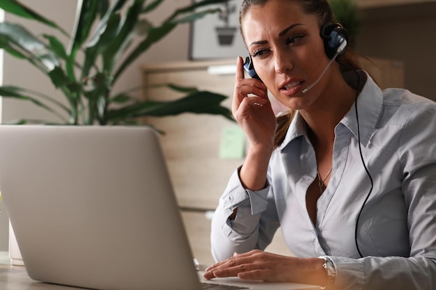 Young call center agent talking to a customer and working on laptop while looking for a solution of the problem