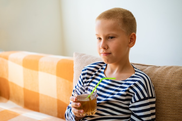 Young calm boy in casual clothes holds fresh juice drink in glass made of glass with a plastic straw...