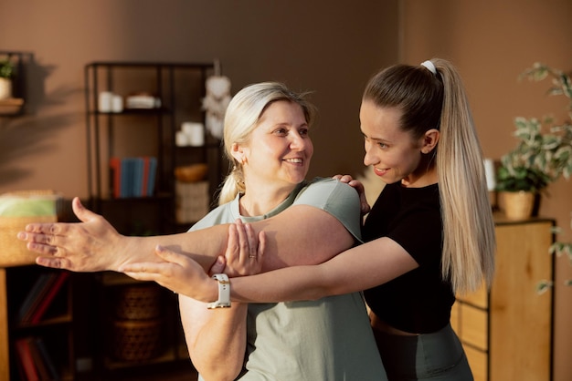 Young caregiver assisting middle aged woman doing exercises stretching standing