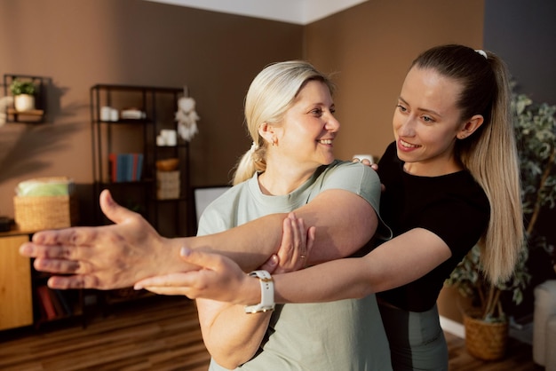 Young caregiver stretching with elderly woman helping doing exercises in the middle of room