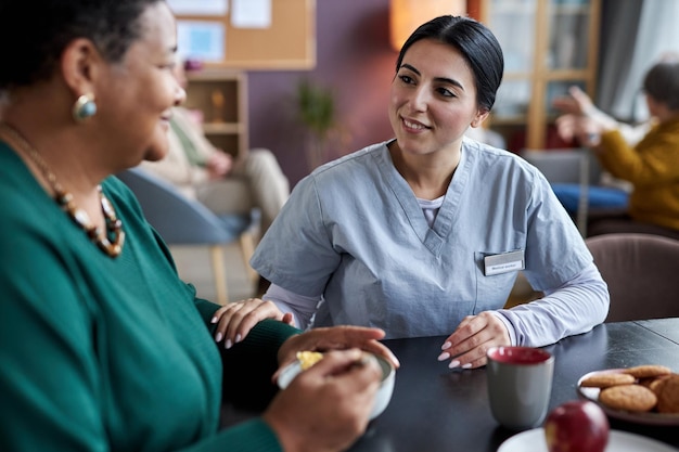 Young caring nurse talking to senior woman at retirement home