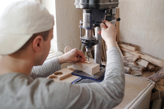 A young carpenter uses a drilling machine to drill holes in a wooden board