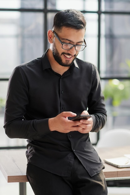 Young casual businessman holding and using smartphone for sms messages