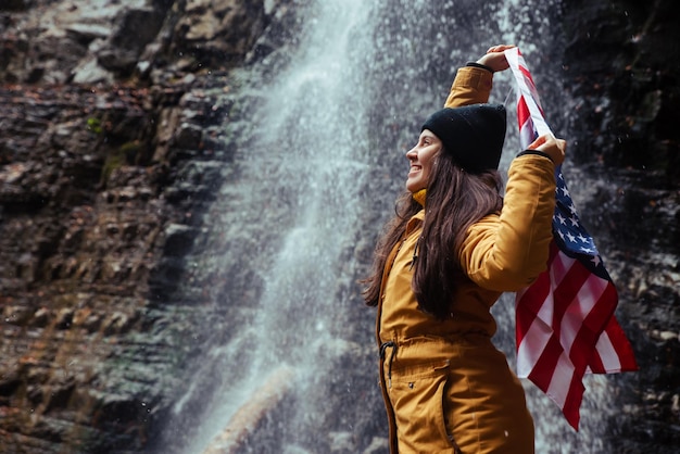 Young caucasian adult female with usa flag in front of waterfall