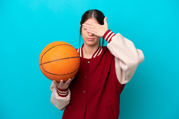 Young caucasian basketball player woman isolated on blue background covering eyes by hands Do not want to see something