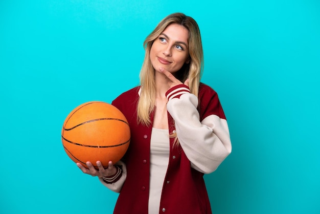 Young caucasian basketball player woman isolated on blue background looking up while smiling