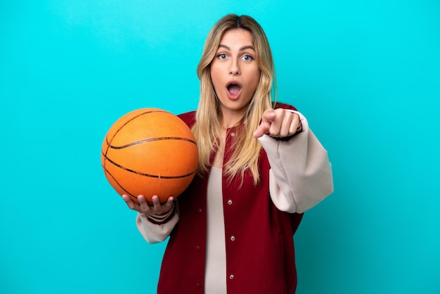 Young caucasian basketball player woman isolated on blue background surprised and pointing front