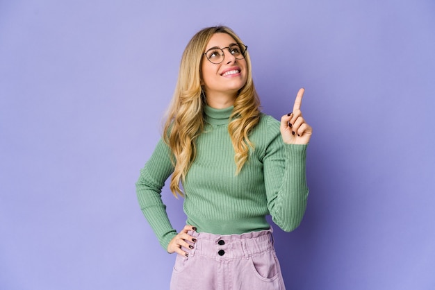 Young caucasian blonde woman indicates with both fore fingers up showing a blank space.