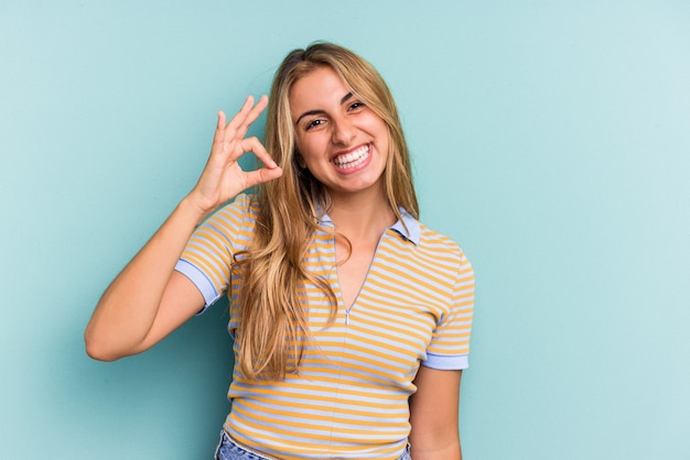 Young caucasian blonde woman isolated on blue background  cheerful and confident showing ok gesture.