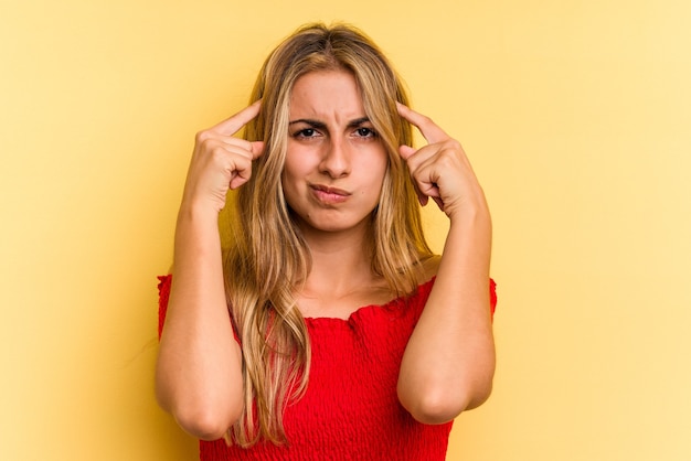 Young caucasian blonde woman isolated on yellow background  focused on a task, keeping forefingers pointing head.