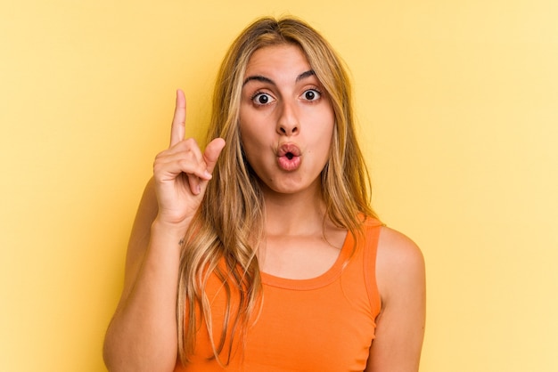 Young caucasian blonde woman isolated on yellow background  pointing upside with opened mouth.