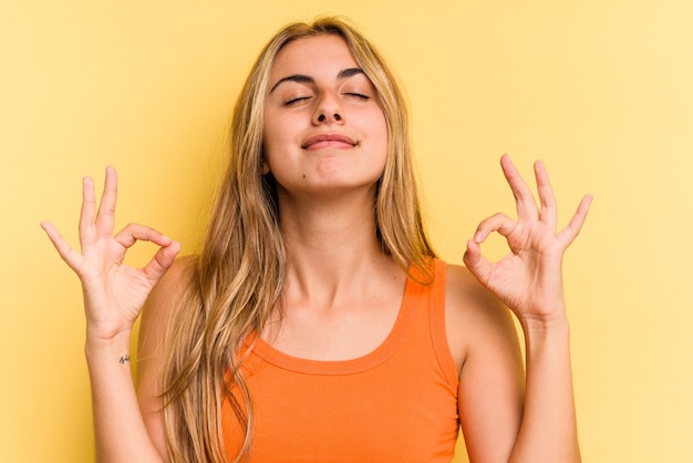 Young caucasian blonde woman isolated on yellow background  relaxes after hard working day, she is performing yoga.