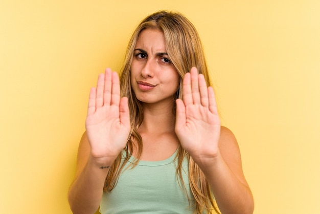 Young caucasian blonde woman isolated on yellow background  standing with outstretched hand showing stop sign, preventing you.