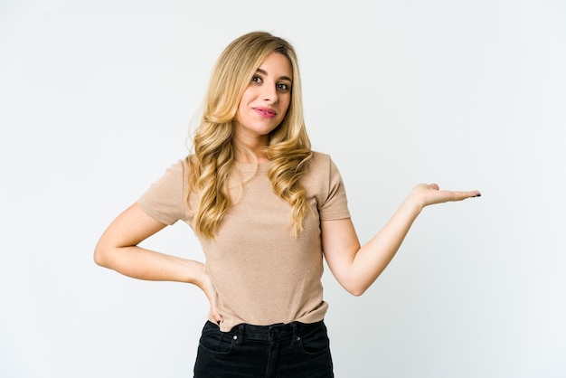 Young caucasian blonde woman showing a copy space on a palm and holding another hand on waist.