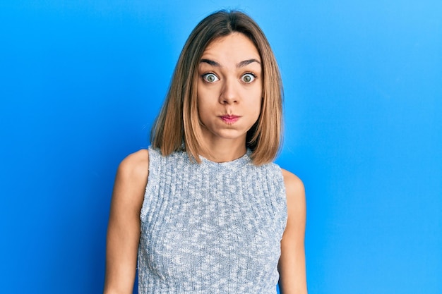 Young caucasian blonde woman wearing casual t shirt puffing cheeks with funny face. mouth inflated with air, crazy expression.