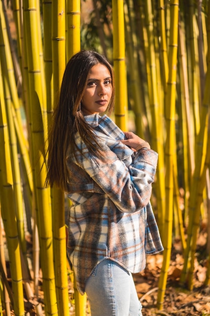 Young Caucasian brunette girl in a plaid wool sweater in a bamboo forest