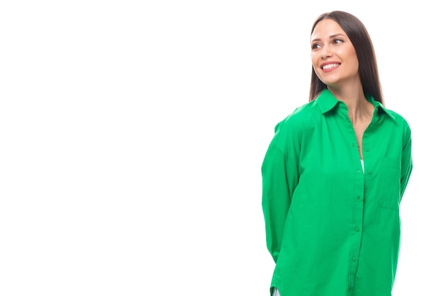 Young caucasian brunette lady with makeup dressed in a green shirt and jeans looks away on a white