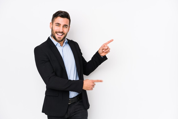 Young caucasian business man against a white wall isolated excited pointing with forefingers away.