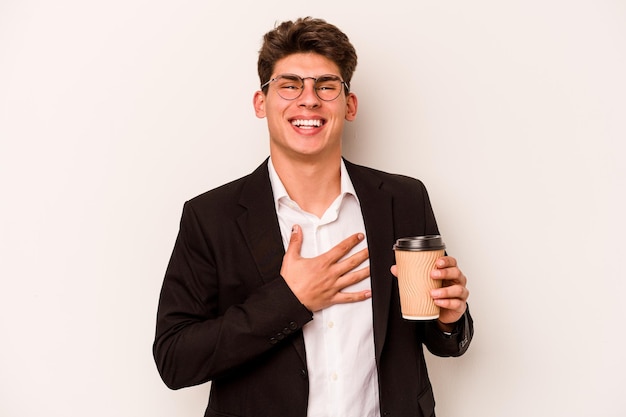 Young caucasian business man holding takeaway coffee isolated on white background laughs out loudly keeping hand on chest