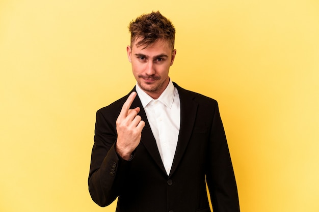 Young caucasian business man isolated on yellow background pointing with finger at you as if inviting come closer.