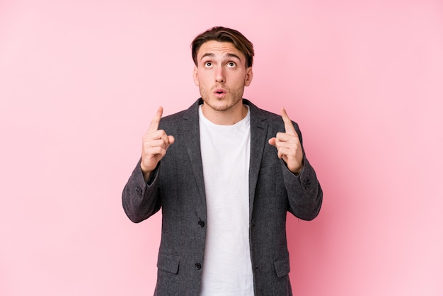 Young caucasian business man posing pointing upside with open mouth.