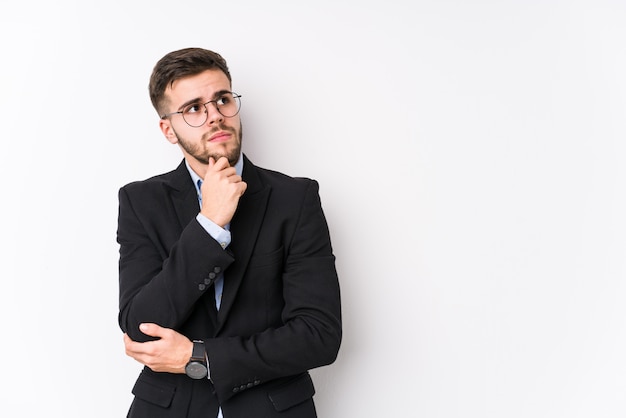 Young caucasian business man posing in a white wall isolated Young caucasian business man looking sideways with doubtful and skeptical expression.