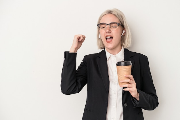 Young caucasian business woman holding take away coffee isolated on white background raising fist after a victory, winner concept.