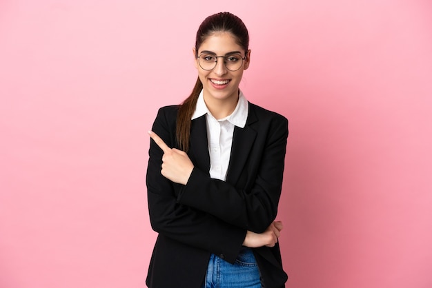 Young caucasian business woman isolated on pink background pointing to the side to present a product