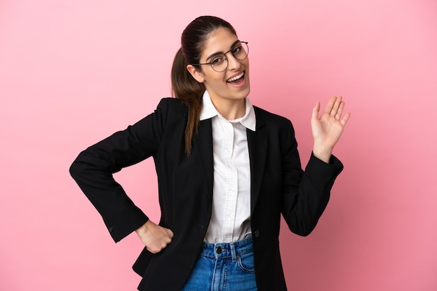 Young caucasian business woman isolated on pink background saluting with hand with happy expression