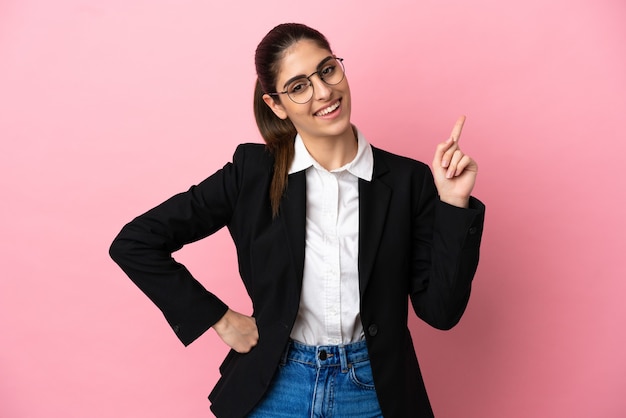 Young caucasian business woman isolated on pink background showing and lifting a finger in sign of the best