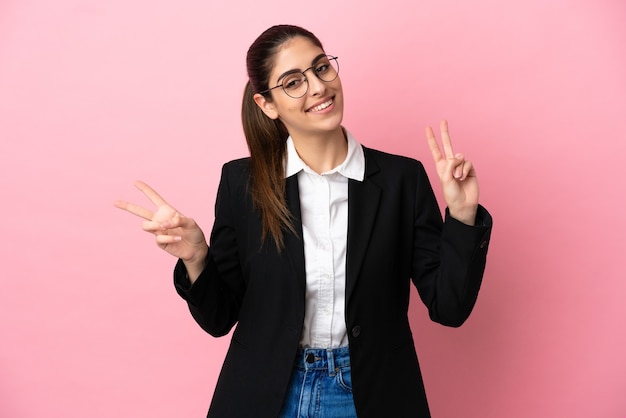 Young caucasian business woman isolated on pink background showing victory sign with both hands