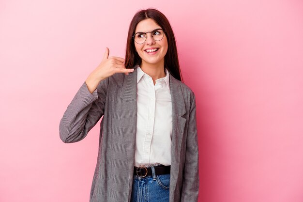 Photo young caucasian business woman isolated on pink wall showing a mobile phone call gesture with fingers.