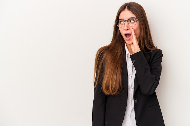 Young caucasian business woman isolated on white background is saying a secret hot braking news and looking aside