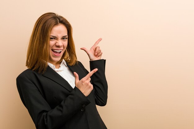 Young caucasian business woman pointing with forefingers to a copy space, expressing excitement and desire.